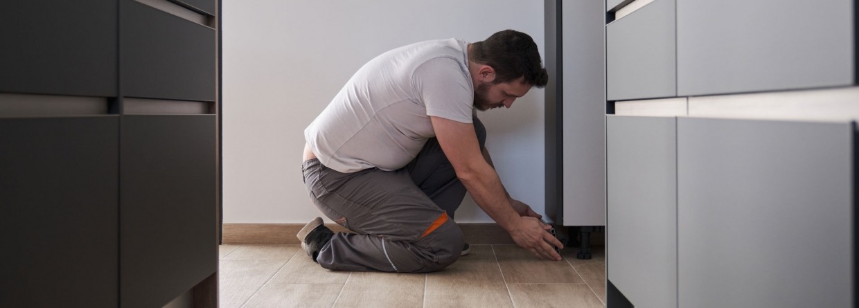 Een jonge man zit geknield in de keuken en is bezig met de vloer