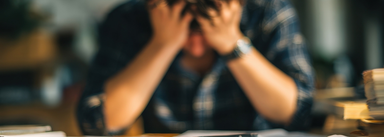 stress; man zit met handen op zijn voorhoogd achter zijn bureau