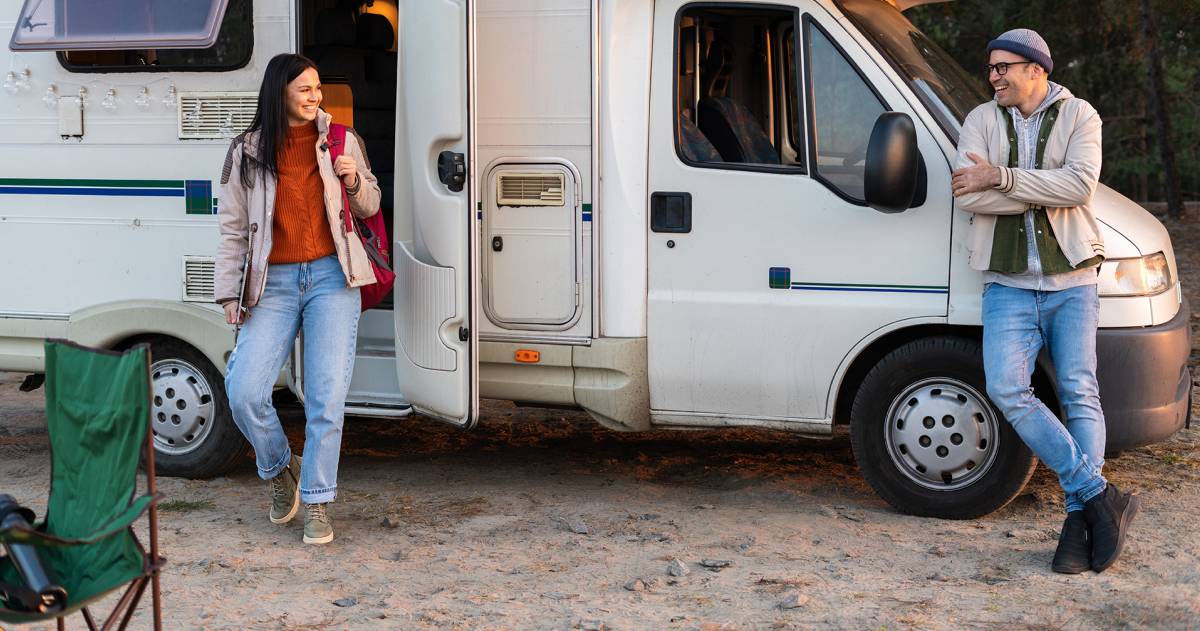 Vrouw komt uit camper in bosrijke omgeving en kijkt haar man vrolijk aan